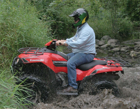 Photo of a man riding an ATV in mud and grass