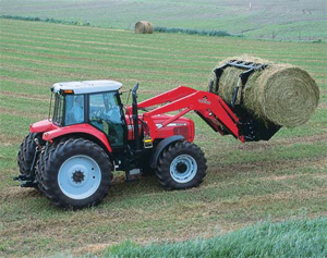 Photo of a red tractor carrying a round hay bale